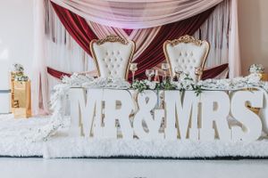 Ornate white wedding stage setup with Mr & Mrs signage and luxurious throne-style chairs.
