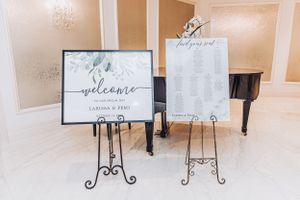 Welcome signs with floral design displayed on decorative metal stands at wedding venue entrance.