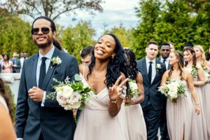 Wedding party members laugh and celebrate while walking in procession at an outdoor ceremony.