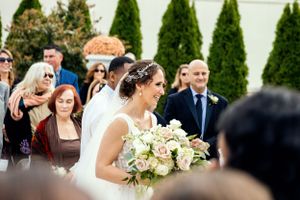 A bride in white dress holds a bouquet of white flowers during an outdoor garden wedding ceremony.