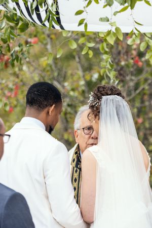Outdoor wedding ceremony under trees with officiant and couple at the altar.