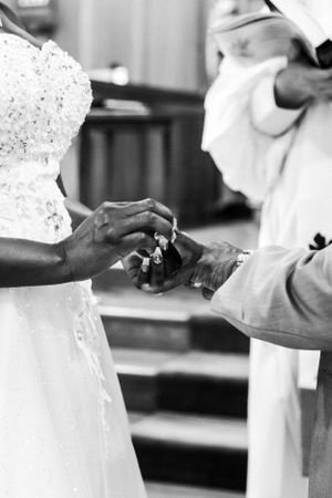 Black and white photo capturing an intimate ring exchange moment during a wedding ceremony.