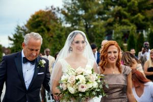 Elegant outdoor wedding procession with white bouquet and formal attire.