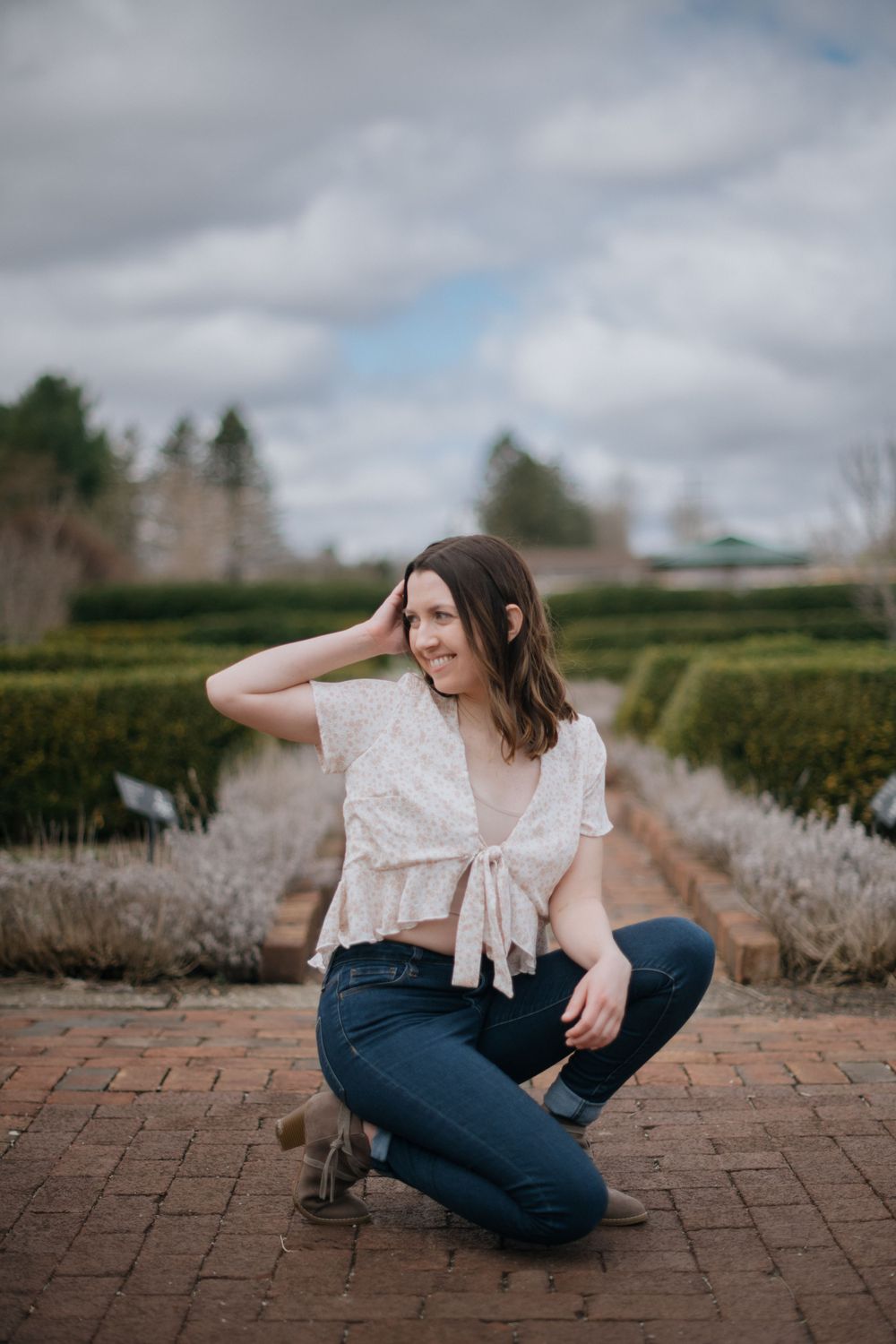 A woman in a white blouse sits on brick pavement in a formal garden setting.
