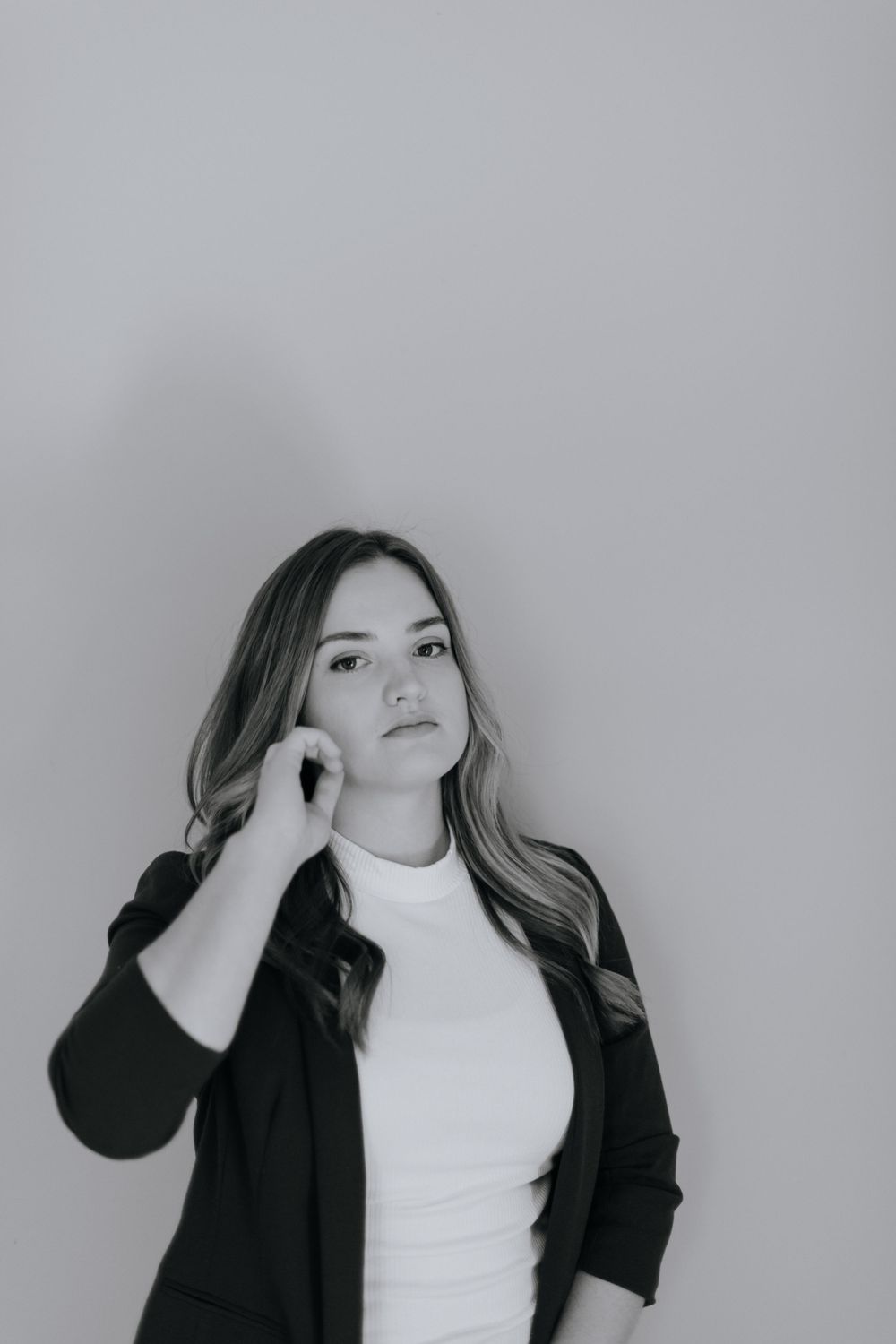 Portrait of person in black blazer and white top against neutral grey background.