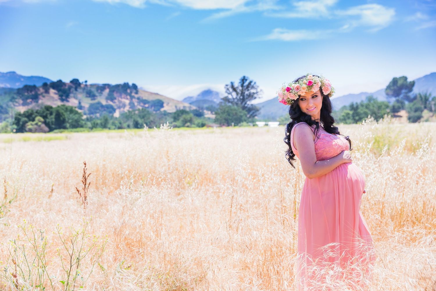 Person in pink dress standing in golden meadow with mountains in background.