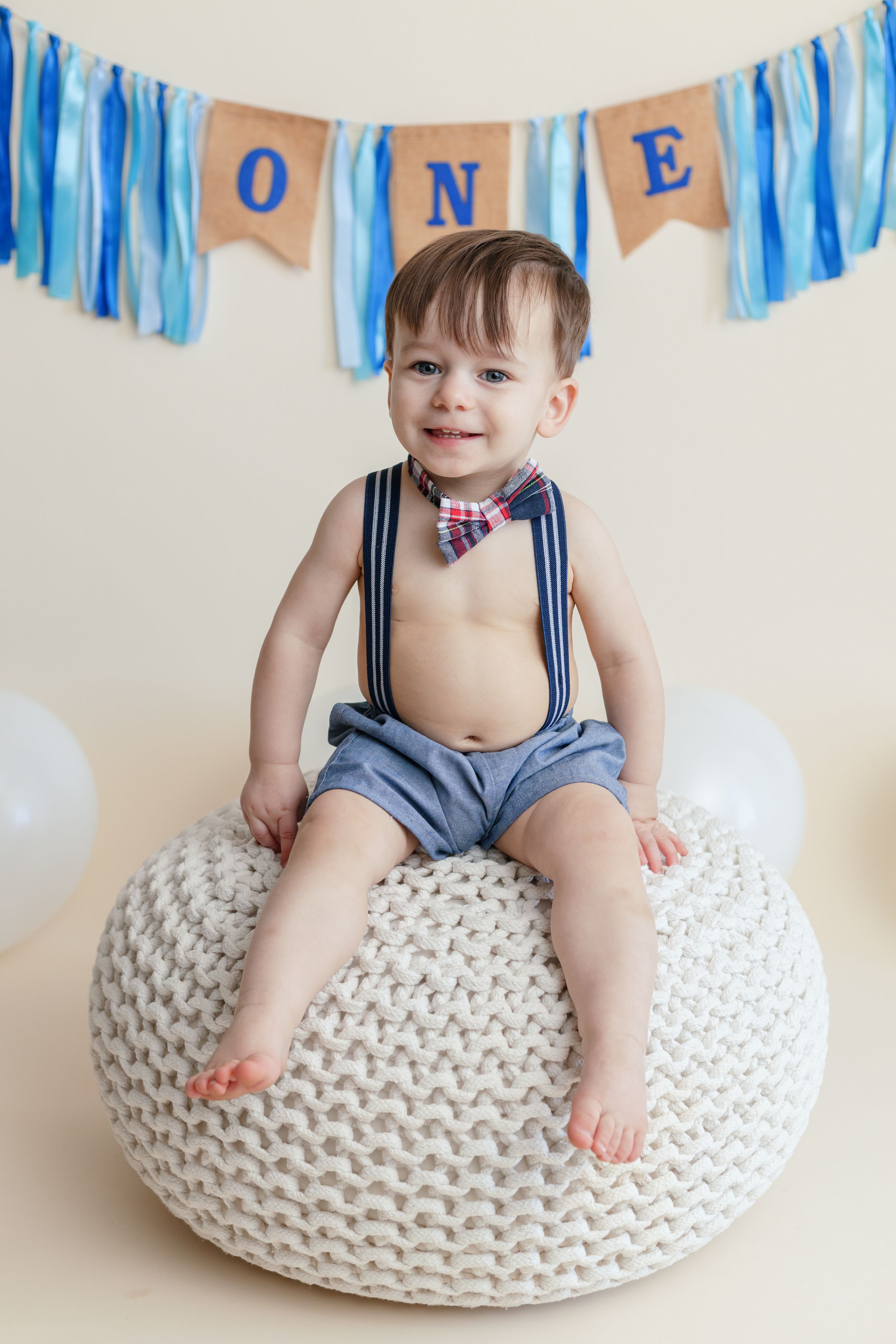 First birthday portrait with blue streamers and 'ONE' banner against white background.