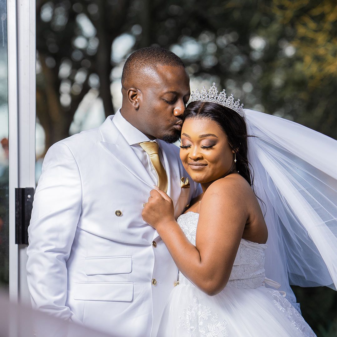 Intimate wedding portrait of couple in white sharing a tender moment under soft lighting.
