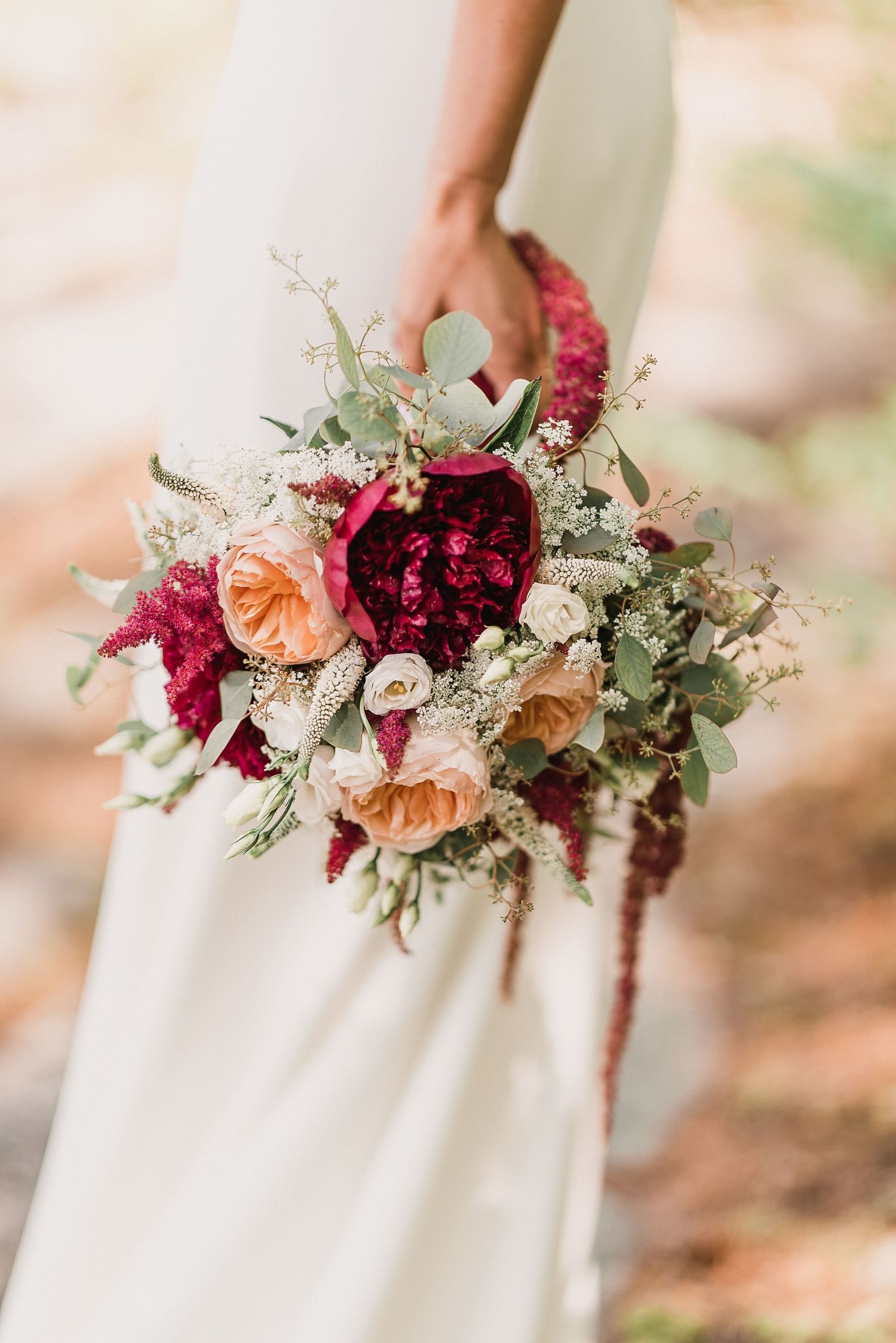 bouquet of deep red and coral flowers held in the hand of bride by Church Island NH wedding Photographer