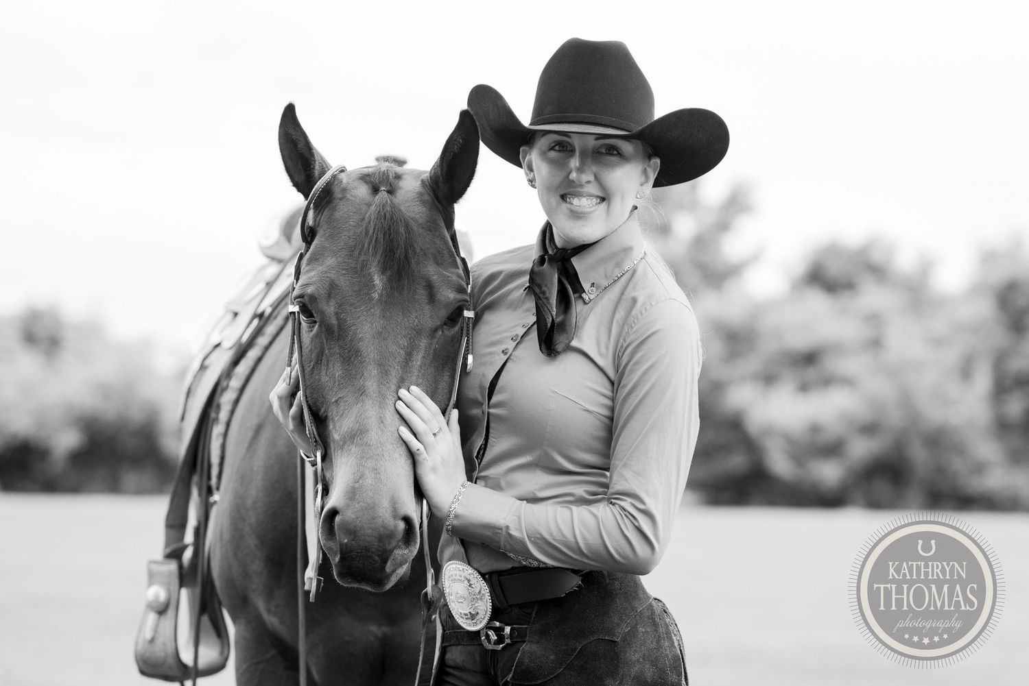 Black and white portrait of horse and rider with western tack in outdoor setting.