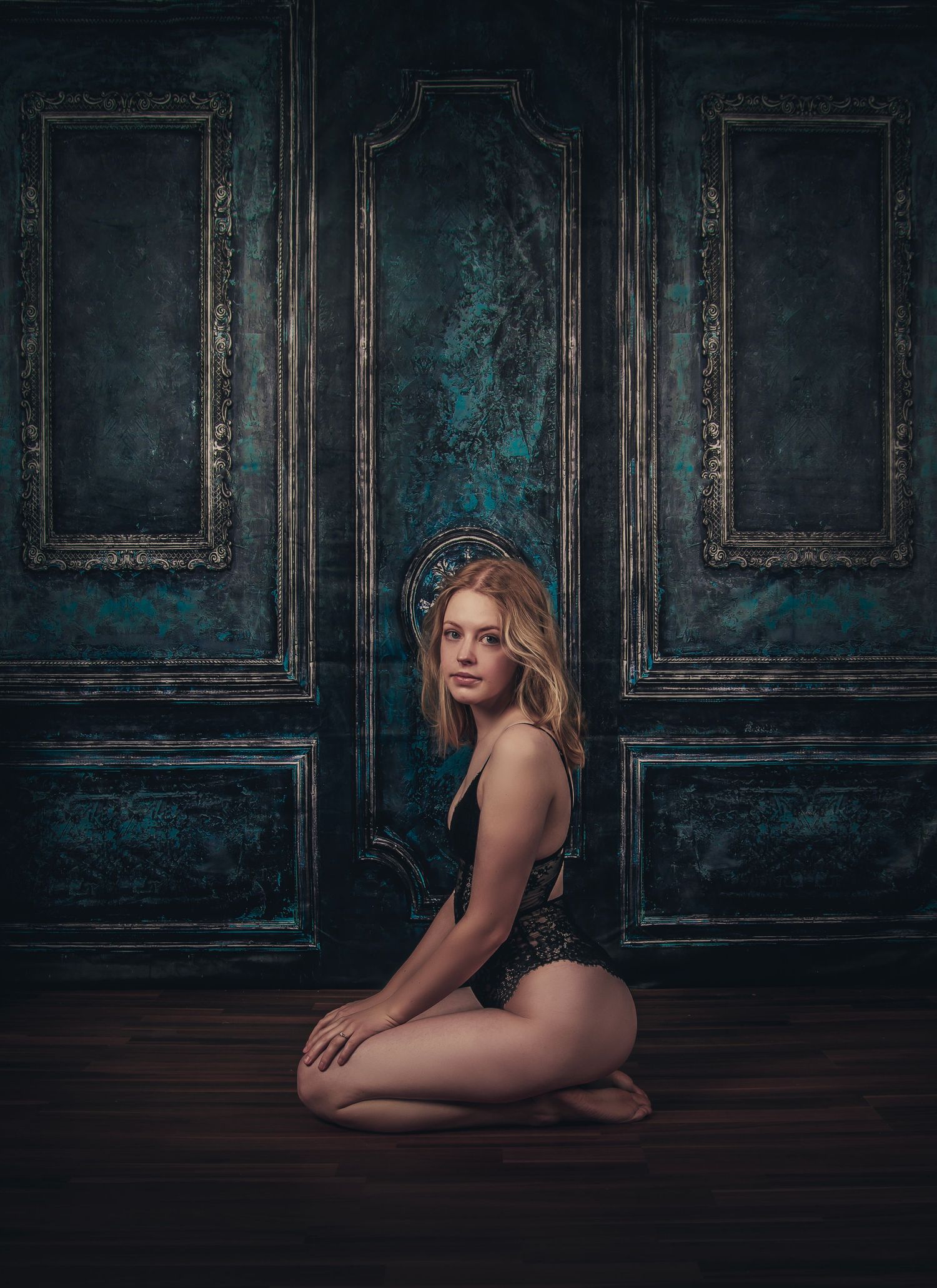 Artistic portrait against vintage blue doors in moody lighting.