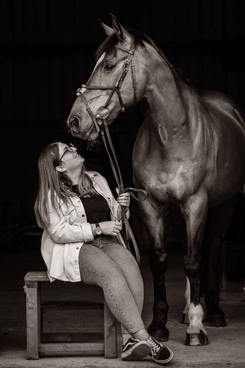 A dramatic black and white portrait of a horse and companion sharing a joyful moment in a barn setting.