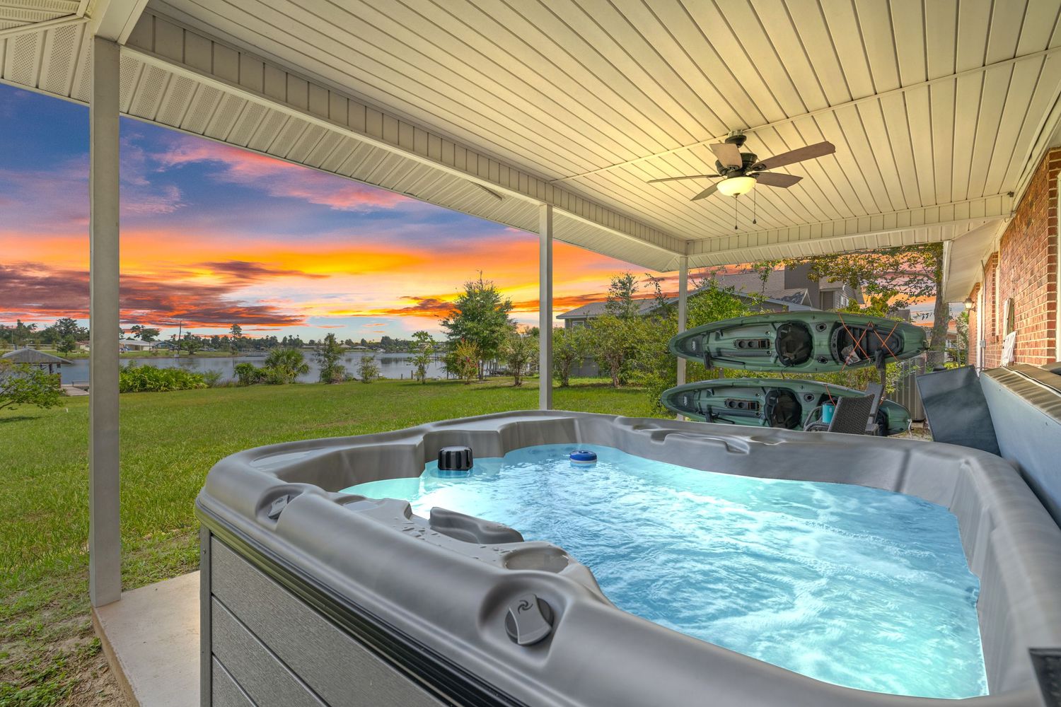 Covered patio with luxury hot tub overlooking waterfront during a dramatic sunset.