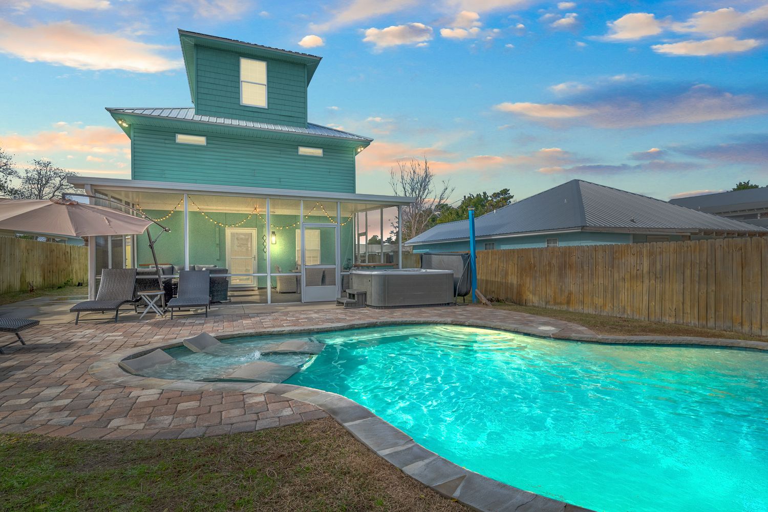 Modern mint-colored beach house with illuminated pool and patio at sunset.