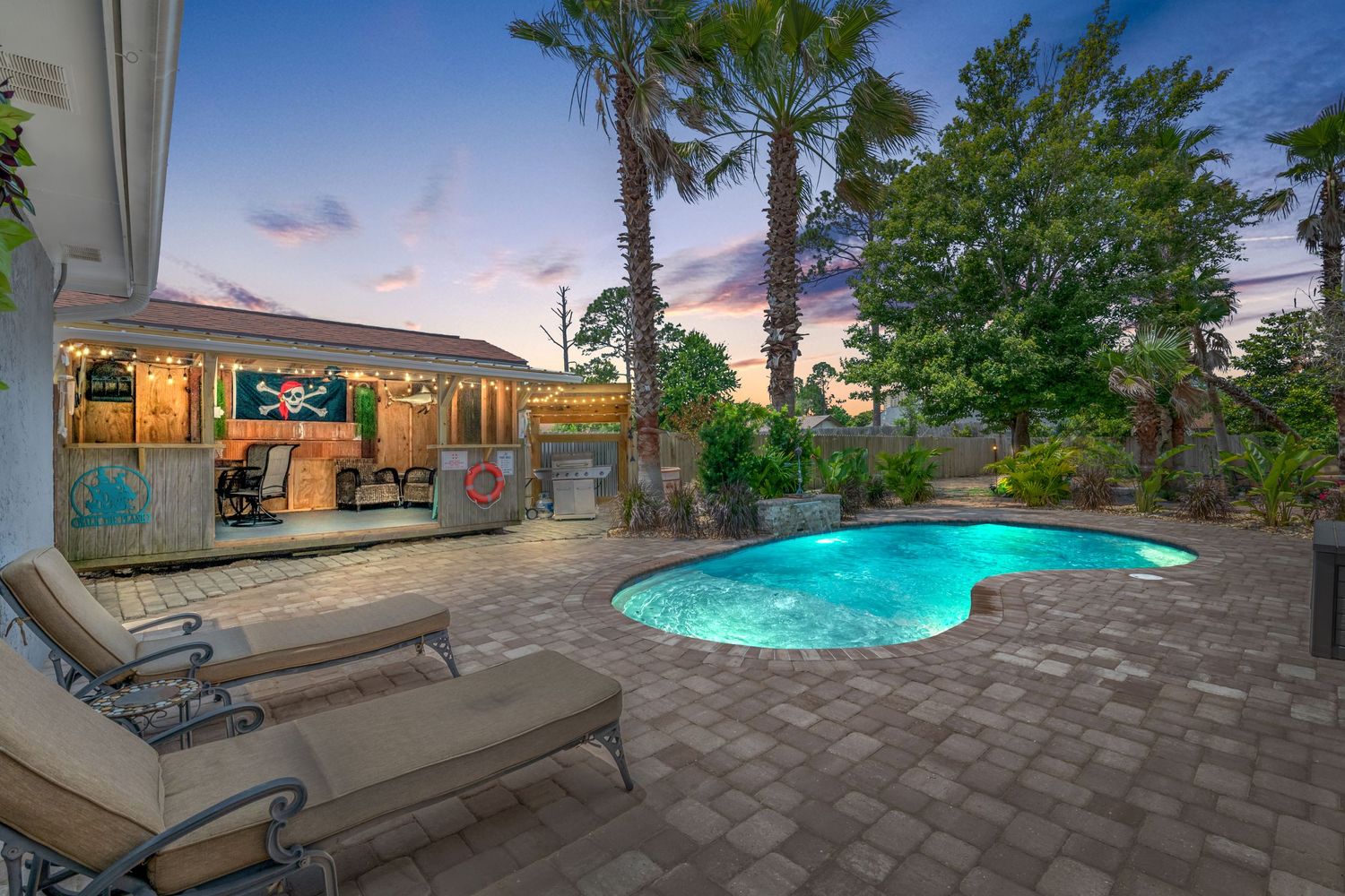 Resort-style backyard with illuminated pool, lounge chairs and covered patio at sunset.