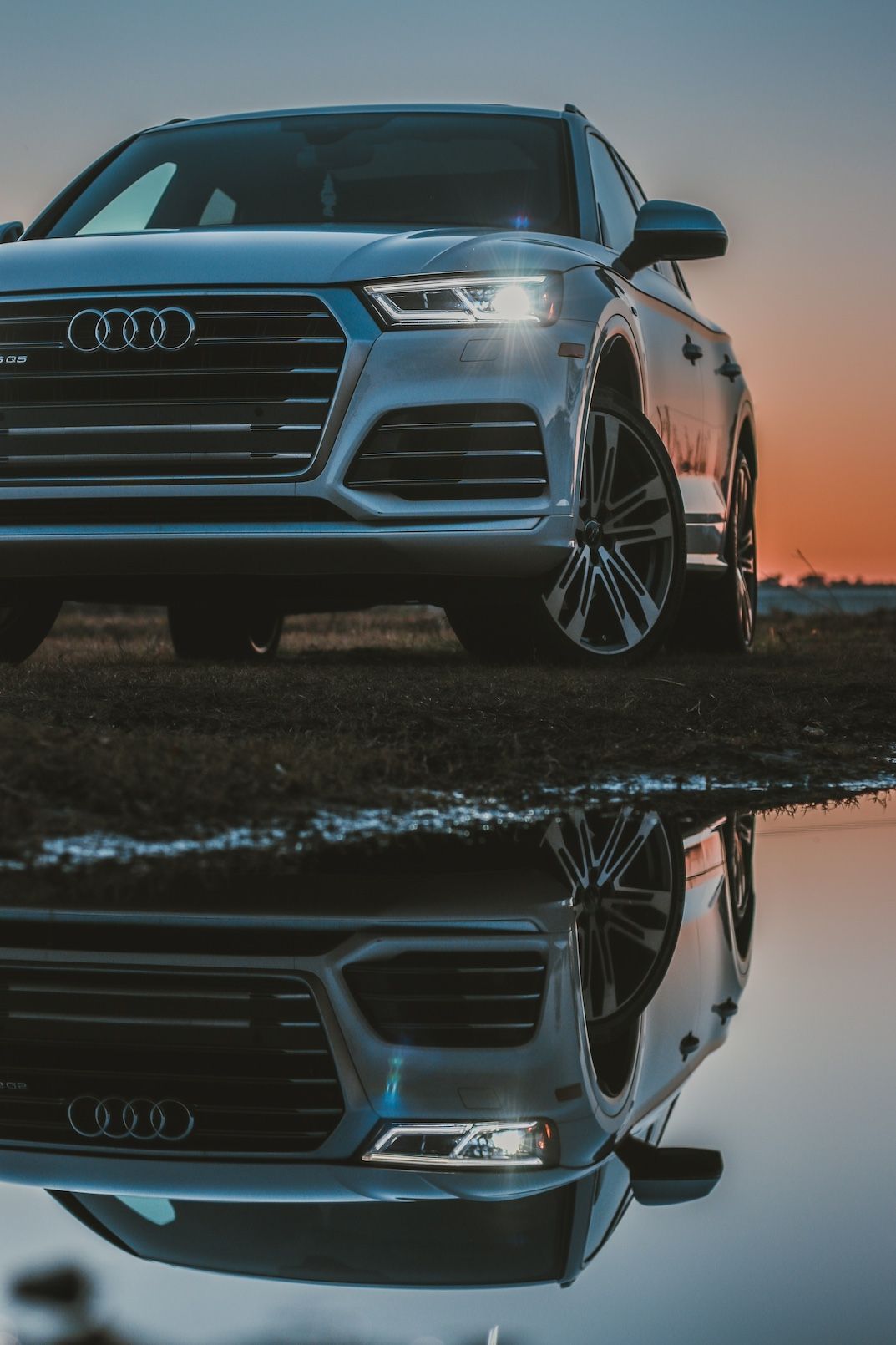 Audi SQ5 SUV front view with reflection in water during golden hour sunset.