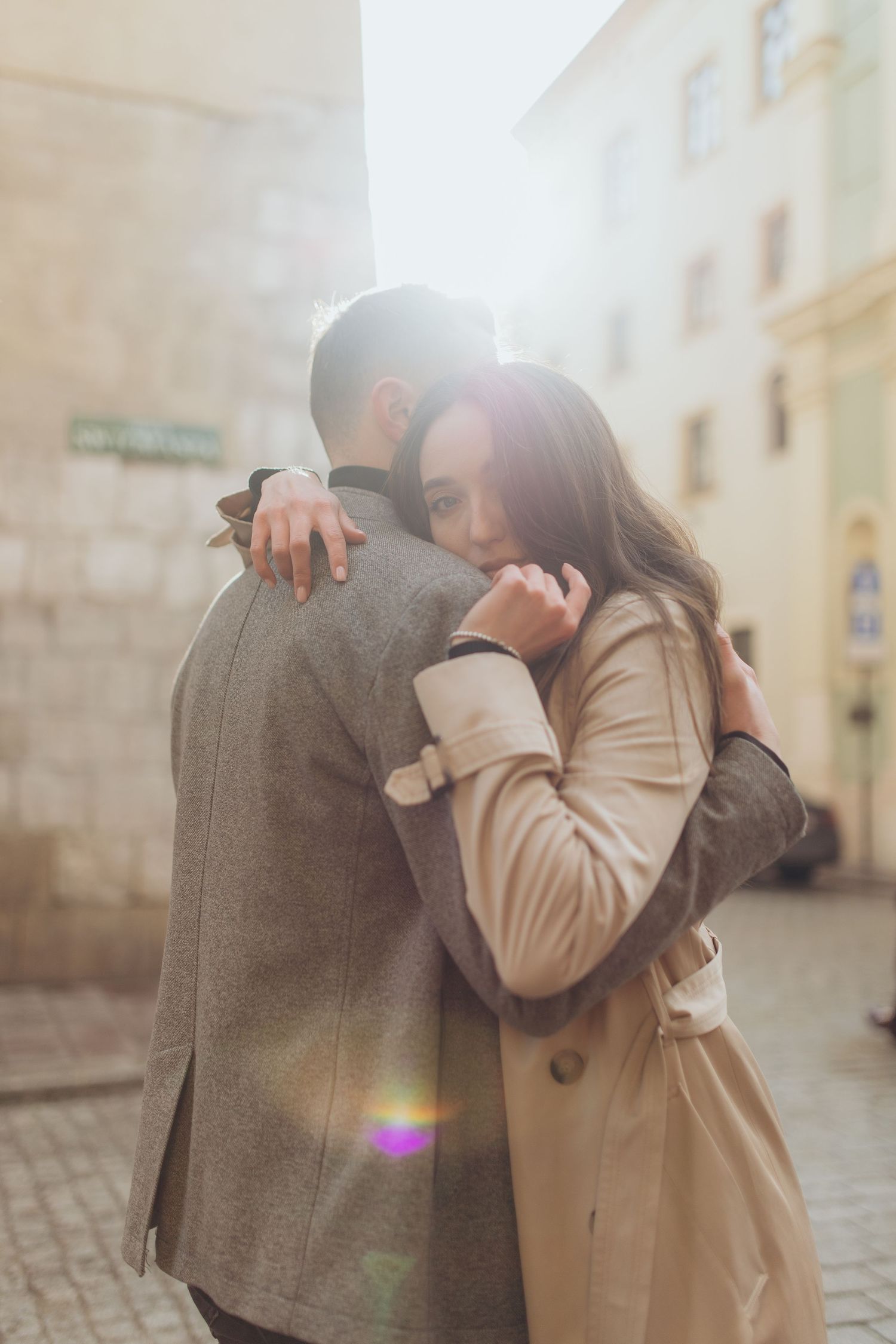 Intimate moment between couple in coats with sun flare on urban street.