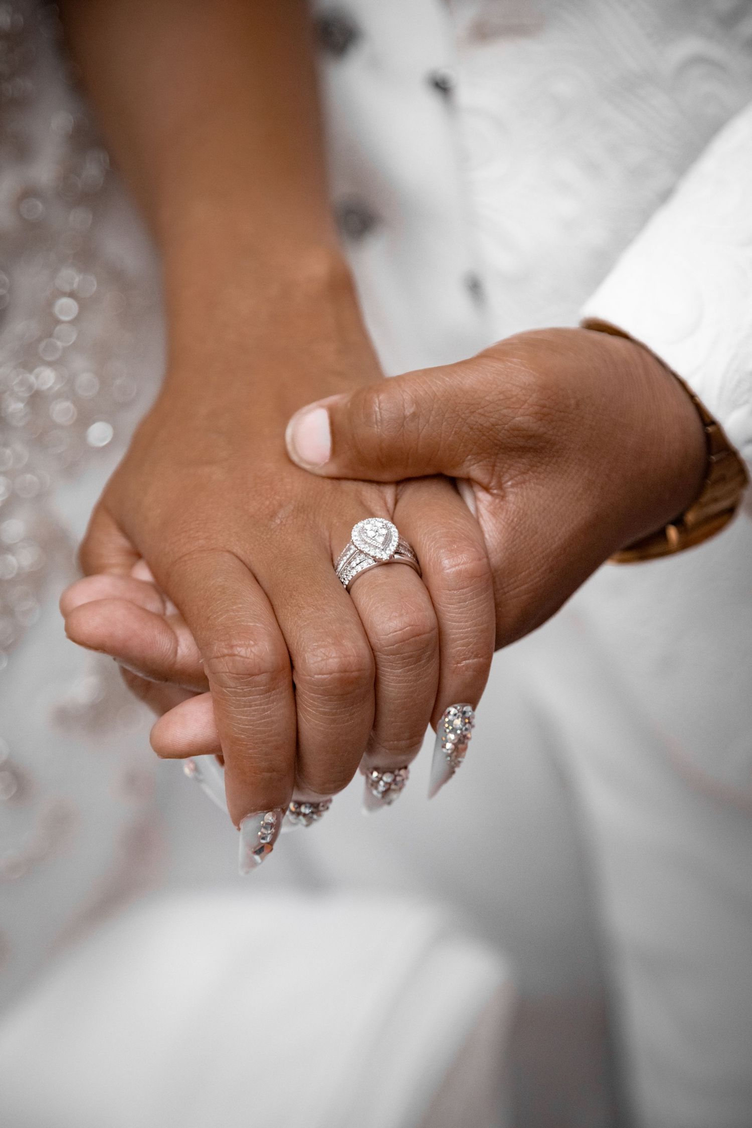 Close-up of clasped hands showing sparkling engagement ring and manicured nails.