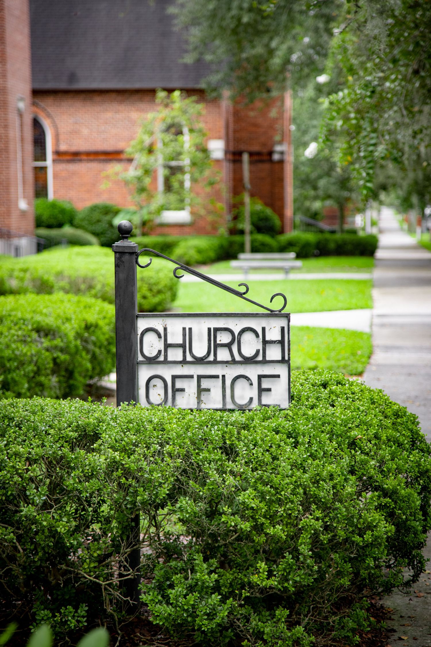 Black church office sign mounted on decorative post with brick building in background.