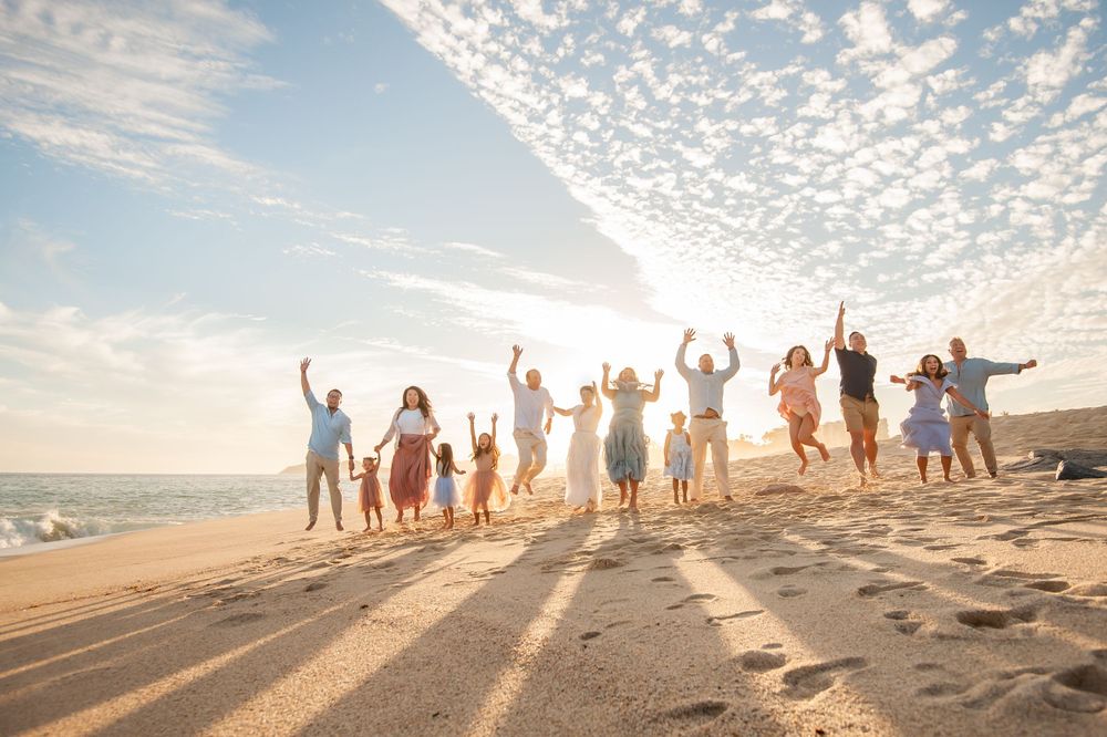 Large group silhouetted against sunset sky on beach with arms raised in celebration.