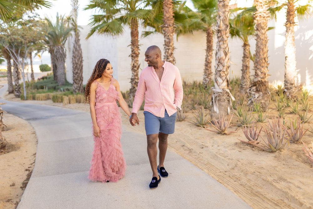 Couple walking along palm tree lined path in coordinated pink and blue outfits.