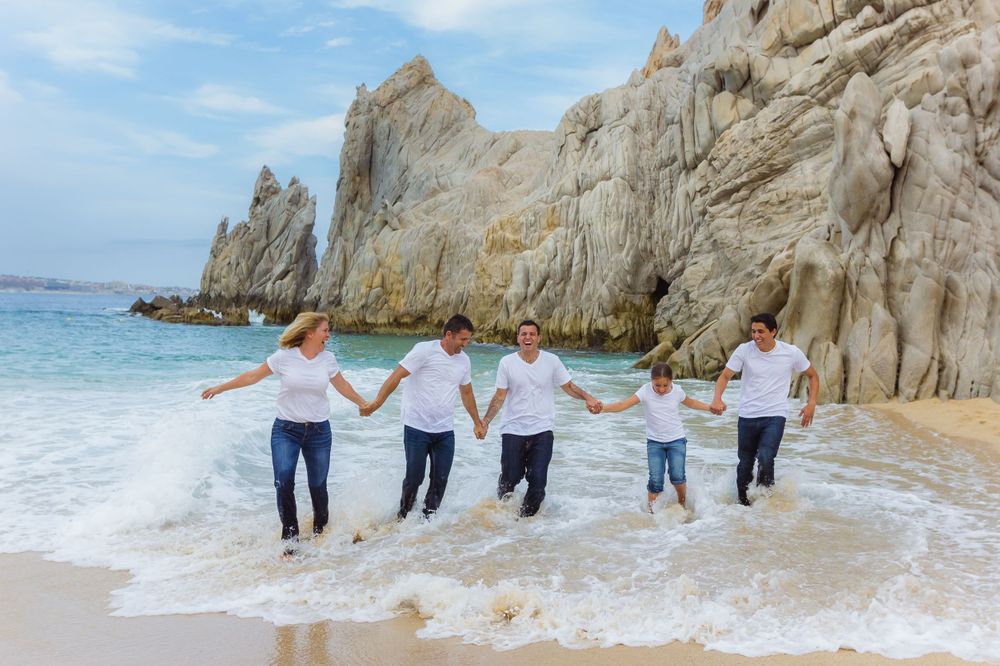 Group walking hand in hand along a beach with rocky cliffs in the background.