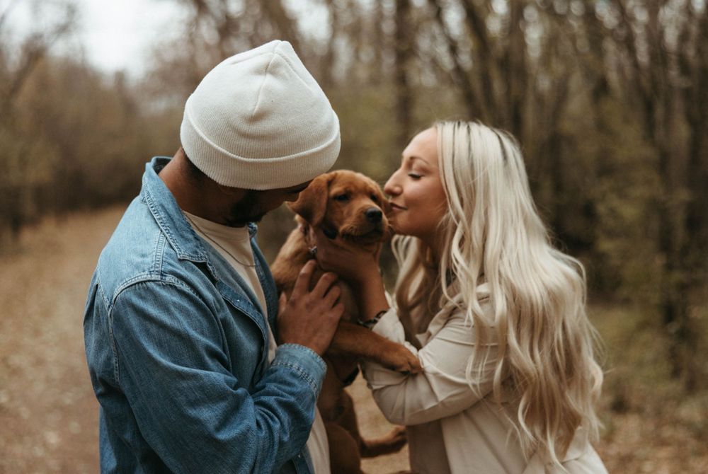 Couple sharing sweet moment with their small brown dog in autumn woodland setting.