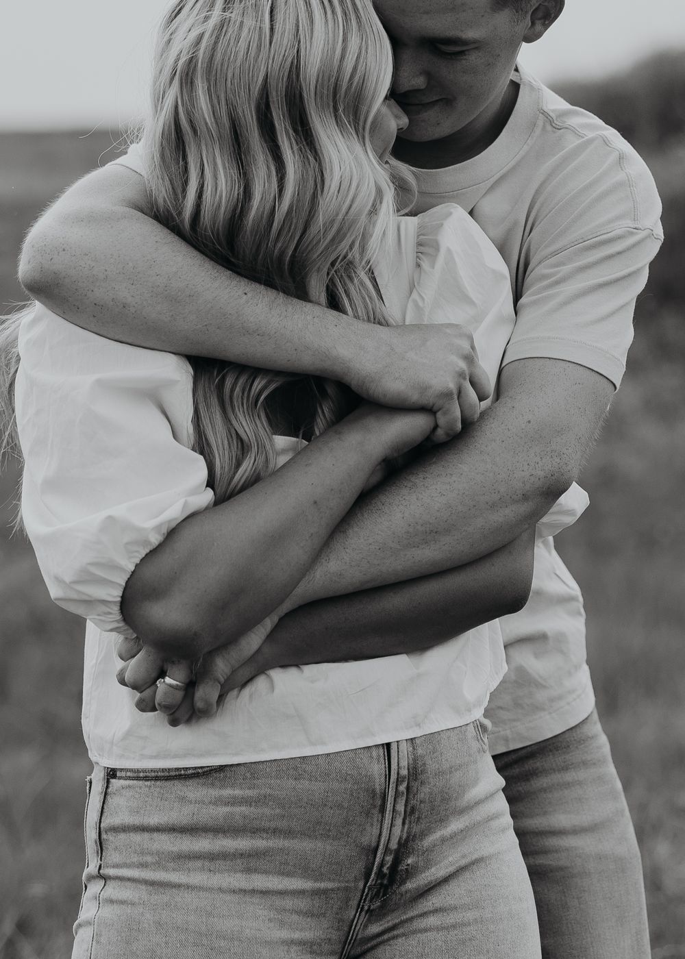 Black and white photo of intimate embrace between couple wearing white shirts and jeans.