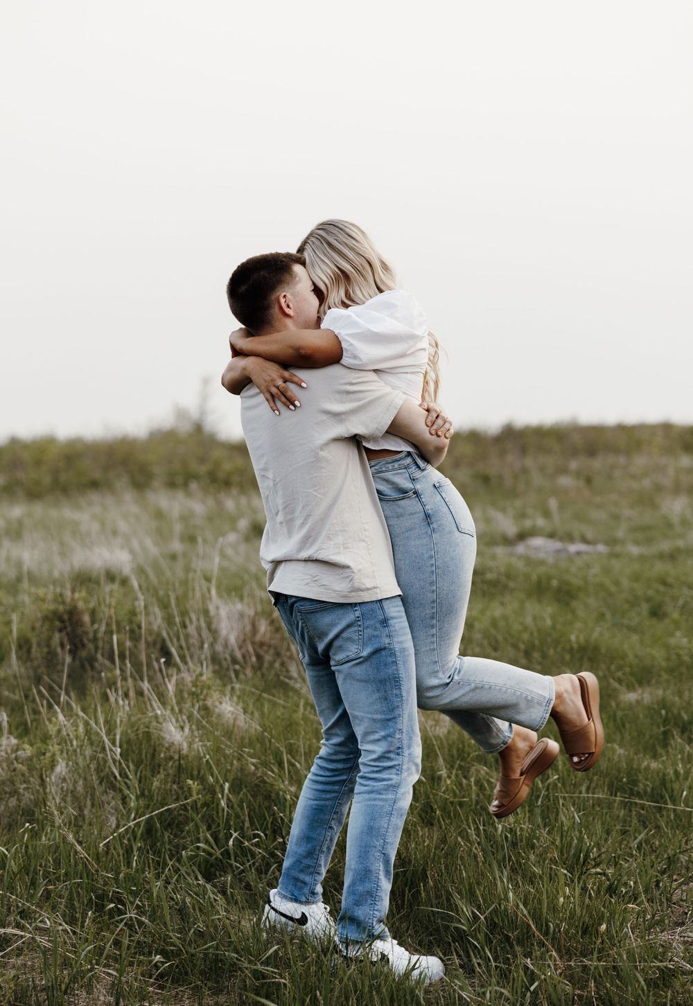 Couple in casual wear hugging and laughing together in a grassy field.