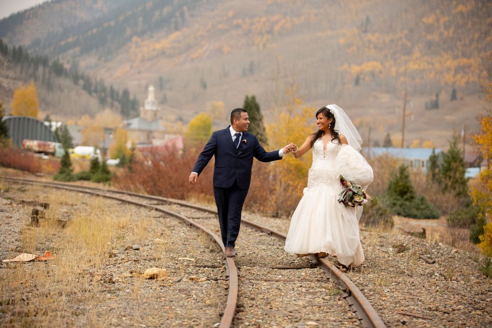 Bride and groom walking hand in hand on railroad tracks with colorful autumn mountains.