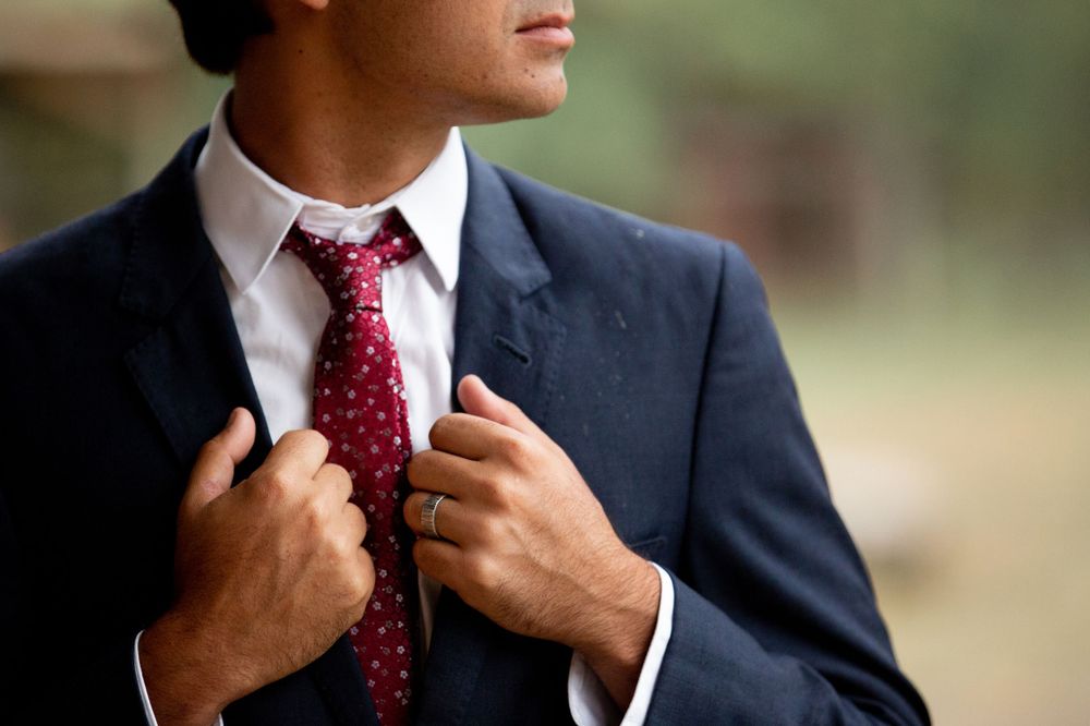 Groom in navy suit adjusts his red polka dot tie in an elegant close-up portrait.