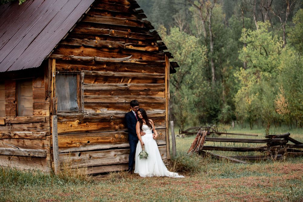 Bride and groom share a romantic moment beside a rustic wooden cabin in autumn setting.