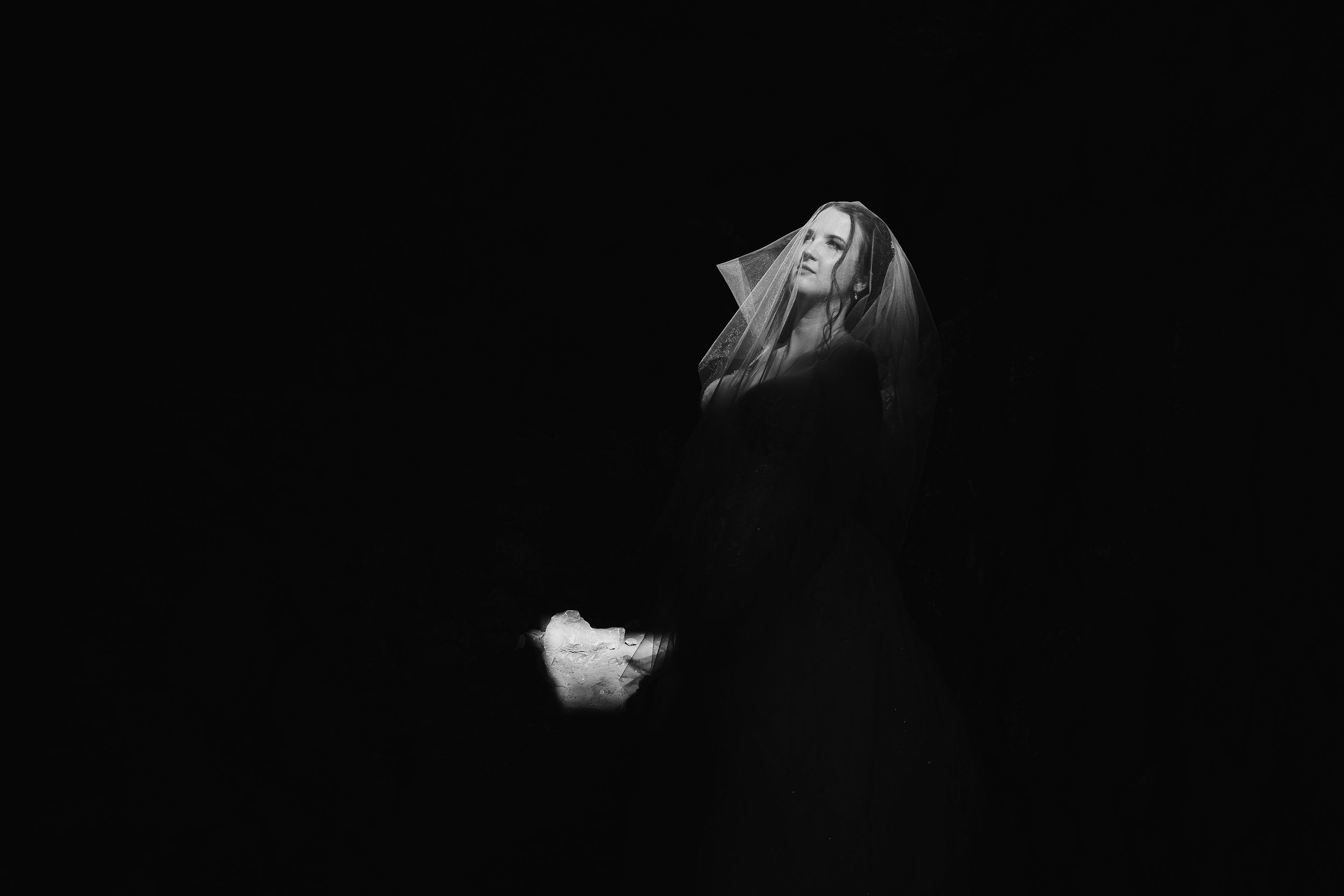 Artistic black and white portrait of a bride against dark background.