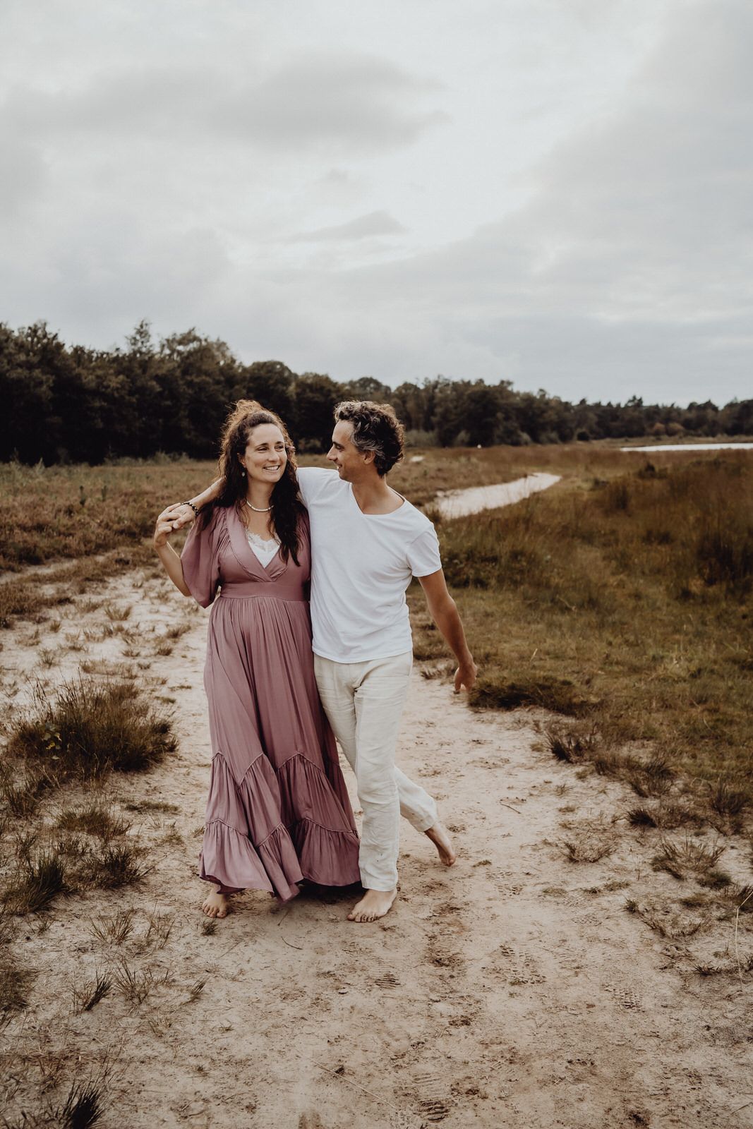 Couple walking together on sandy path through natural landscape.