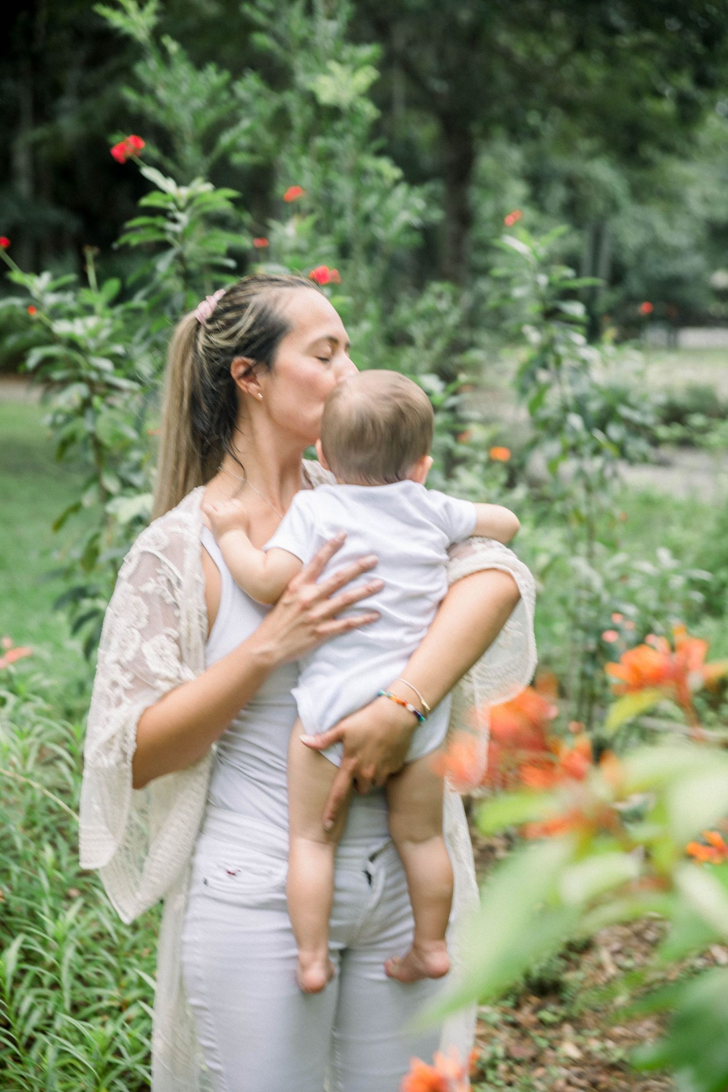 A tender moment captured in a garden with orange flowers as a woman in white lace holds a small child.