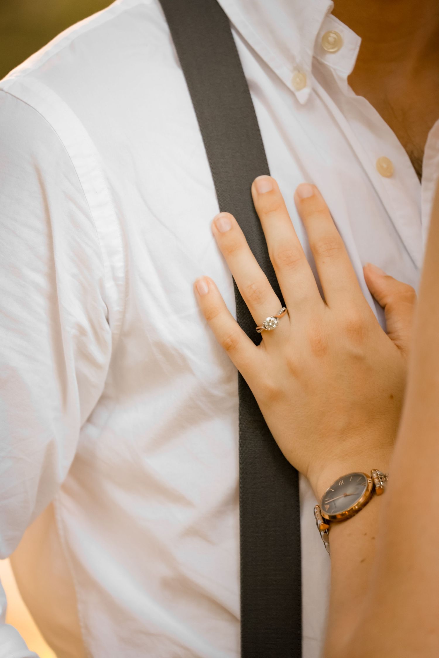 Close-up of hand wearing engagement ring against white shirt with suspenders.