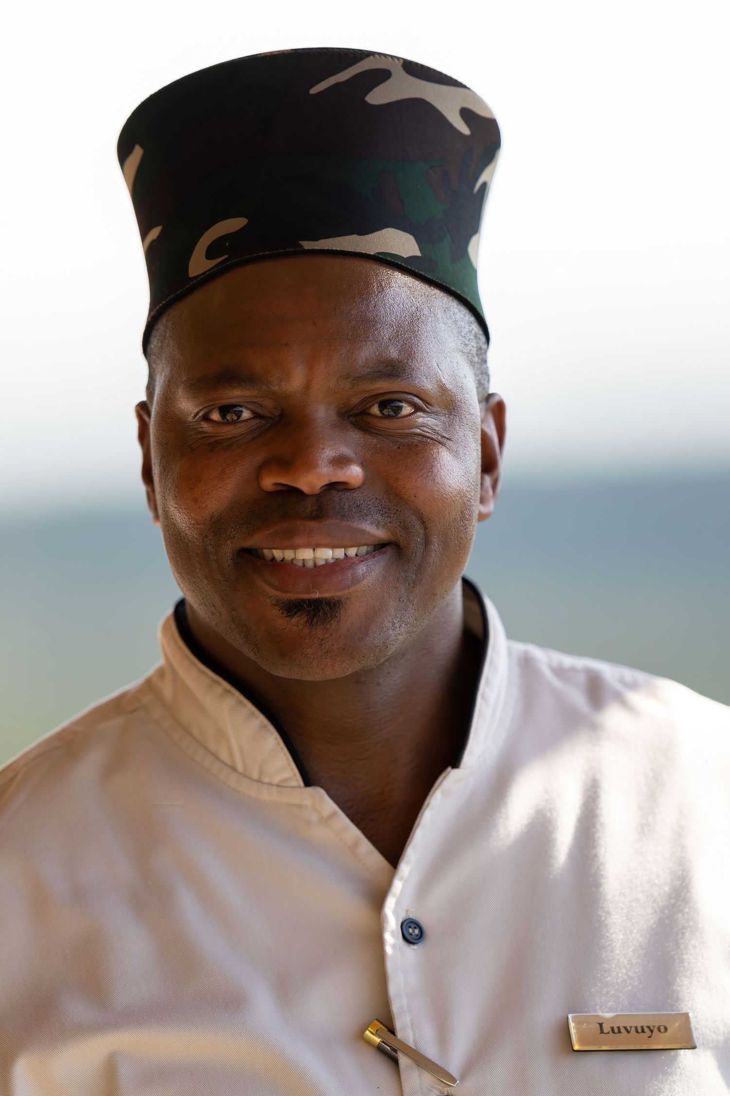 A person in a black cap and white uniform smiling at the camera.