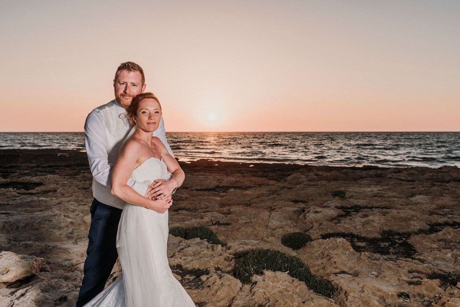 A romantic sunset beach photo with waves and rocky shoreline creating a stunning wedding backdrop.