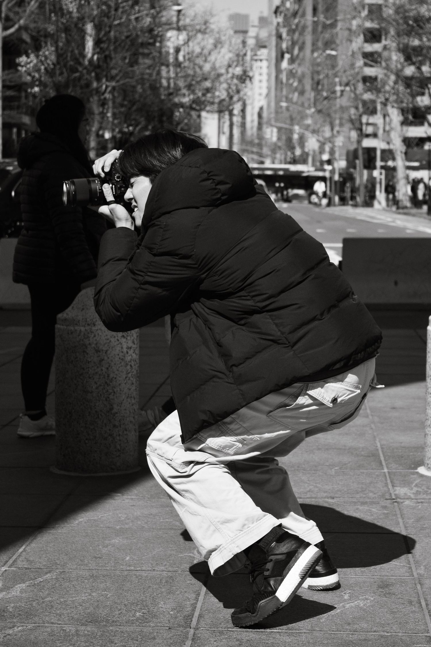 Black and white sequence showing a figure crouching down in an urban street setting.