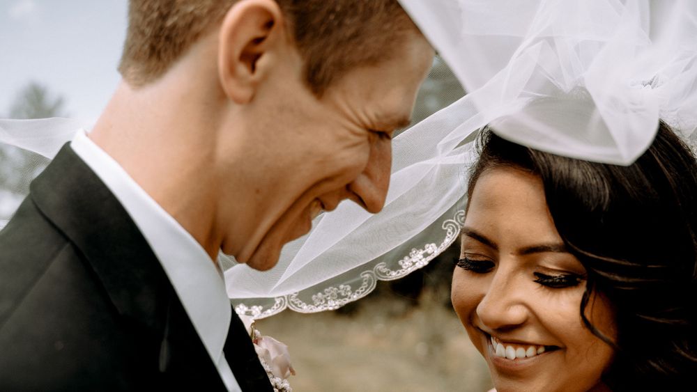 A joyful wedding moment with a couple sharing an intimate smile under a delicate white veil.