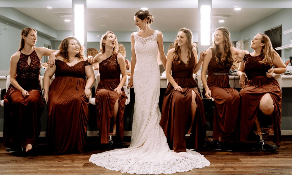 A bride in white standing with her bridesmaids wearing burgundy dresses in a wedding photoshoot.