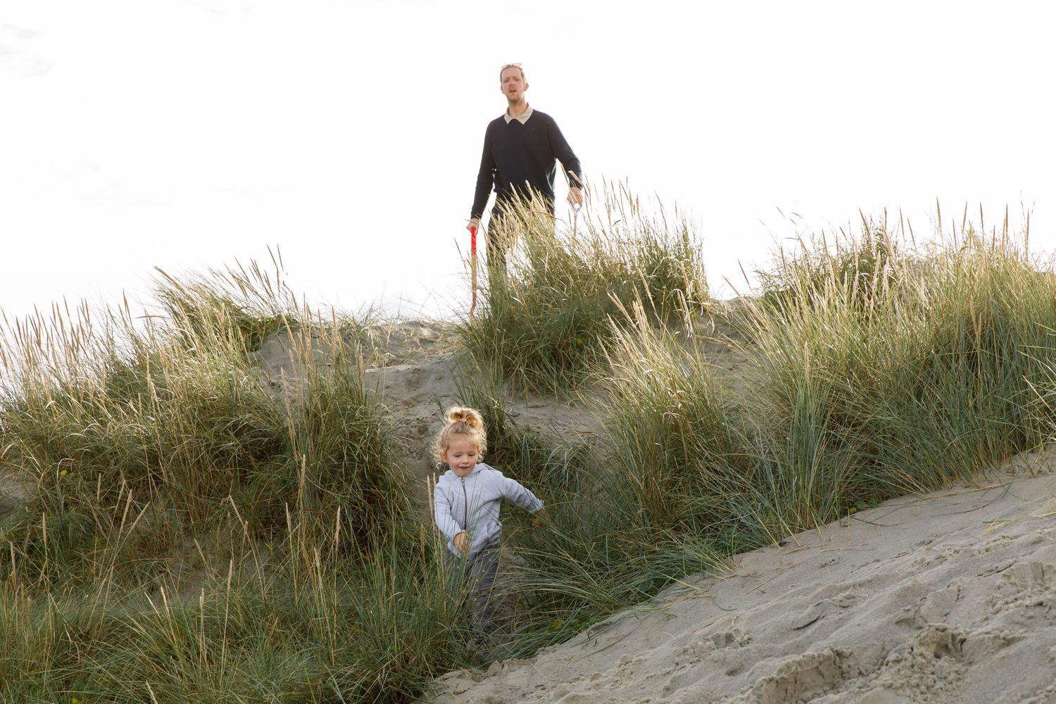 Two people explore sandy dunes covered in tall beach grass during a family beach photoshoot