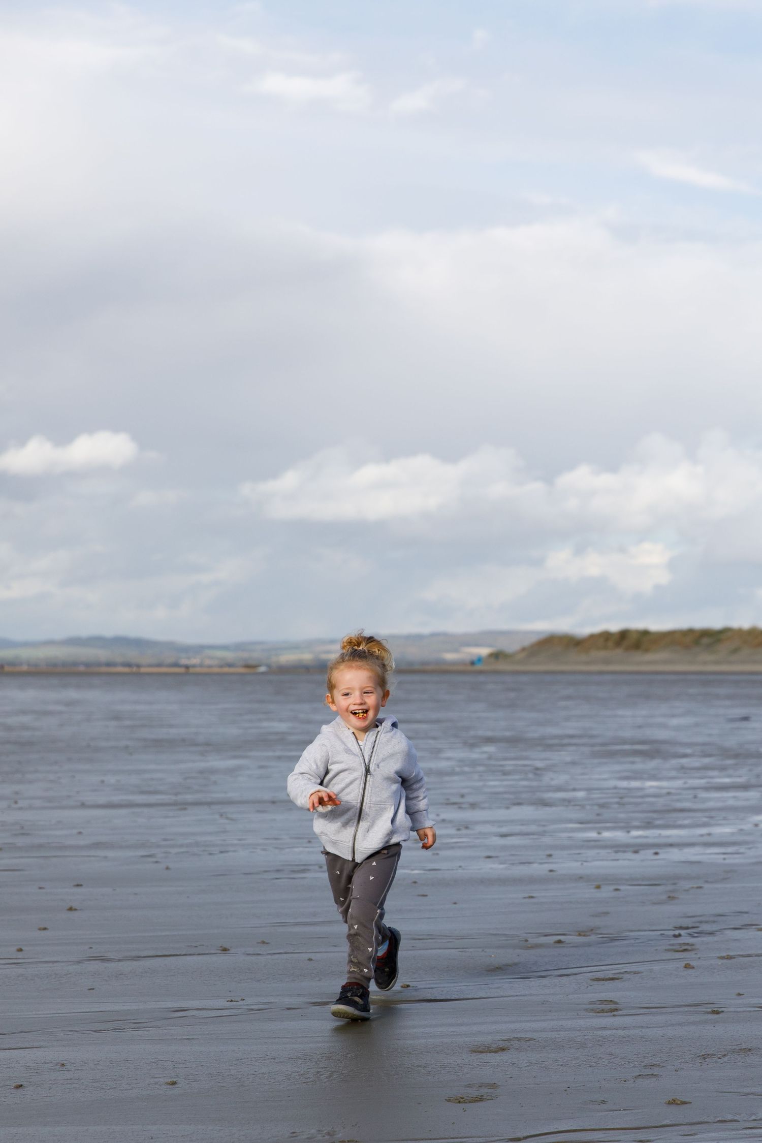 Child running joyfully on a scenic beach with cloudy skies in the background during a family beach photoshoot