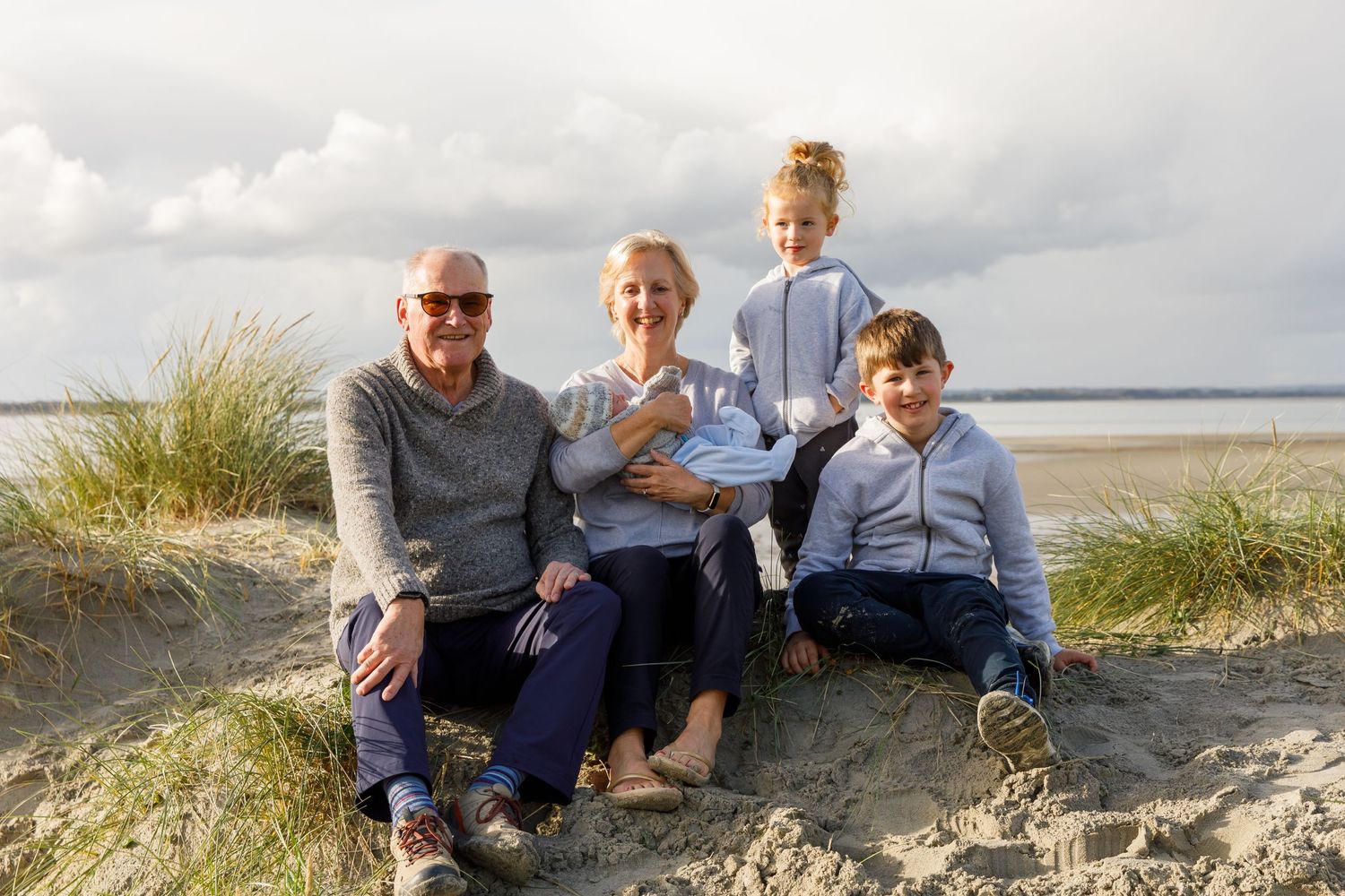 A group sits together on a sandy dune overlooking the ocean during a family beach photoshoot