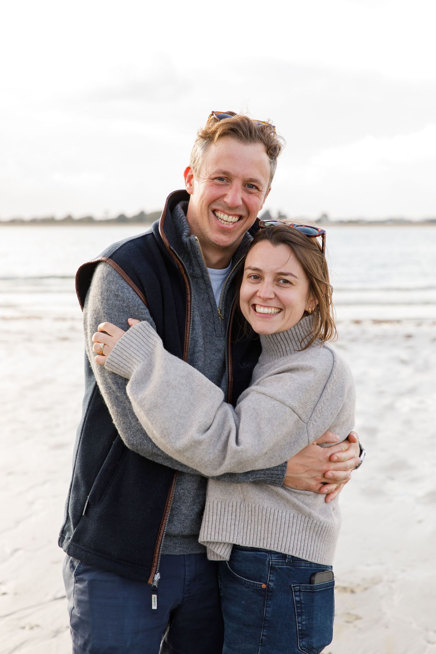 Couple embracing and smiling warmly on a beach with overcast skies during a family beach photoshoot