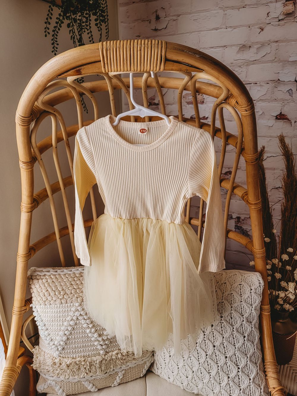 Cream ribbed knit bodice with tulle skirt long sleeve toddler dress hanging on rattan chair.