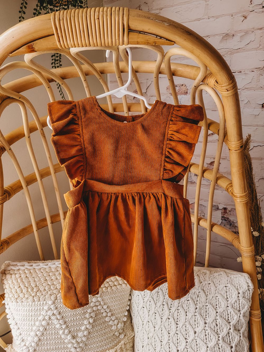 Rust brown muslin ruffle flutter sleeve toddler dress with pockets on rattan chair.