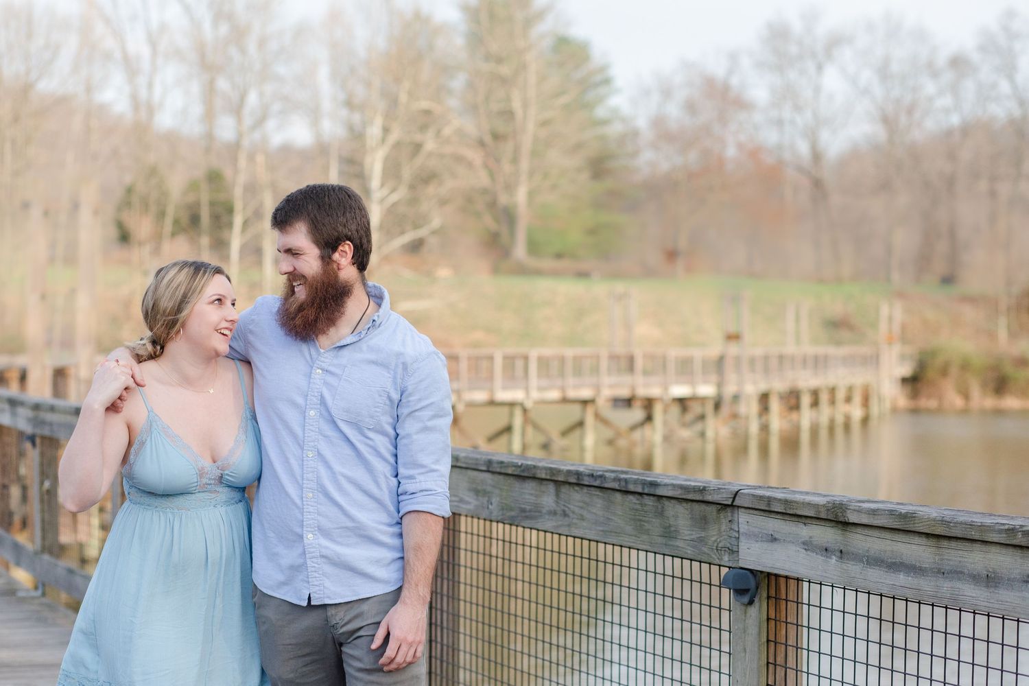 A couple embracing on a wooden boardwalk overlooking a scenic lake.