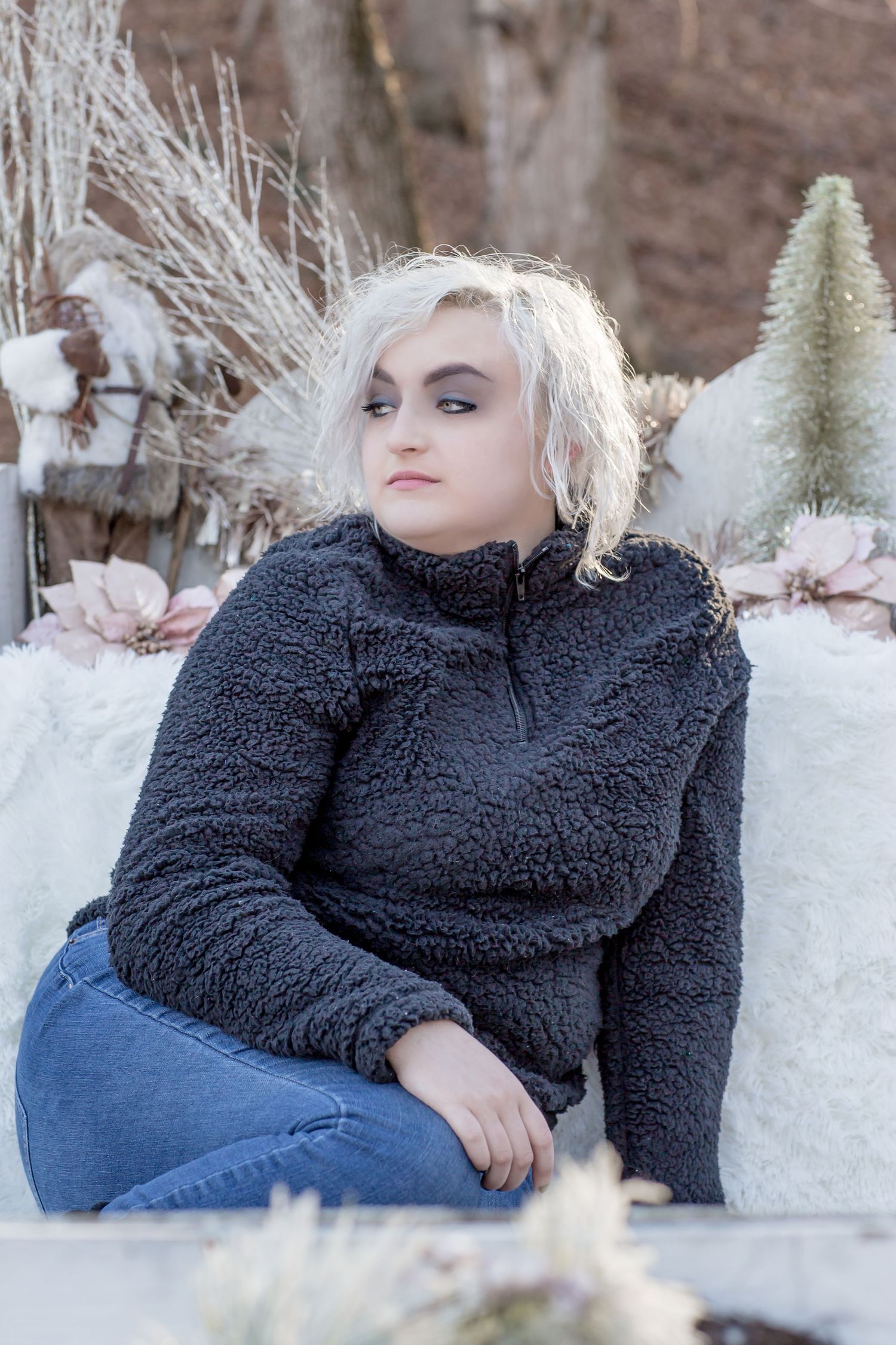 Young woman with platinum blonde hair wearing a gray sherpa pullover sitting outdoors in winter.