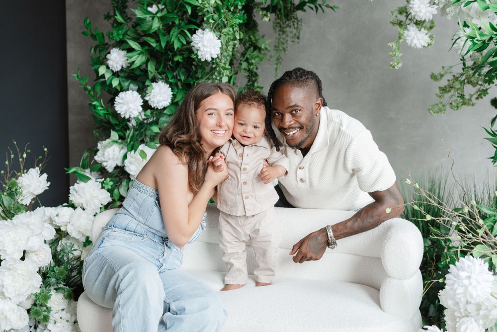 Mint room photographer family session in Toronto, capturing smiling family and toddler standing on couch at floral setup